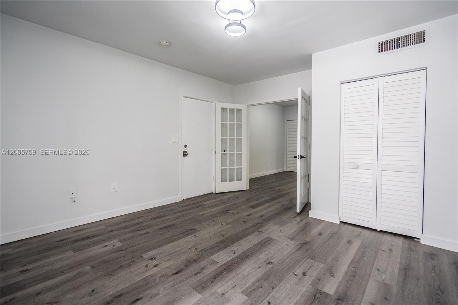 An empty room features white walls, gray wood-look flooring, a closet, and French doors — 920 Pennsylvania Ave # 206, Miami Beach FL 33139, MIAMI BEACH, FL