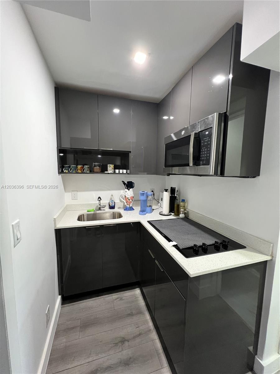 A small kitchen features dark gray glossy cabinets, white countertops, and a stainless steel microwave — 2847 Polk St # 2, Hollywood FL 33020, HOLLYWOOD, FL