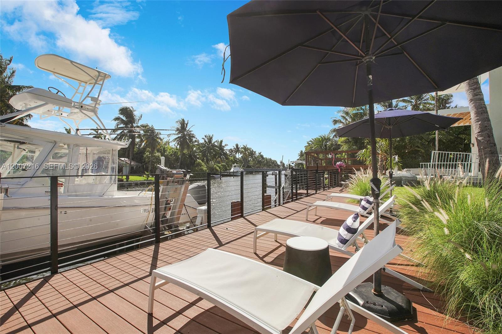 A wooden deck features lounge chairs and umbrellas beside a boat docked in a canal — 815 NE 76th St, Miami FL 33138, MIAMI, FL