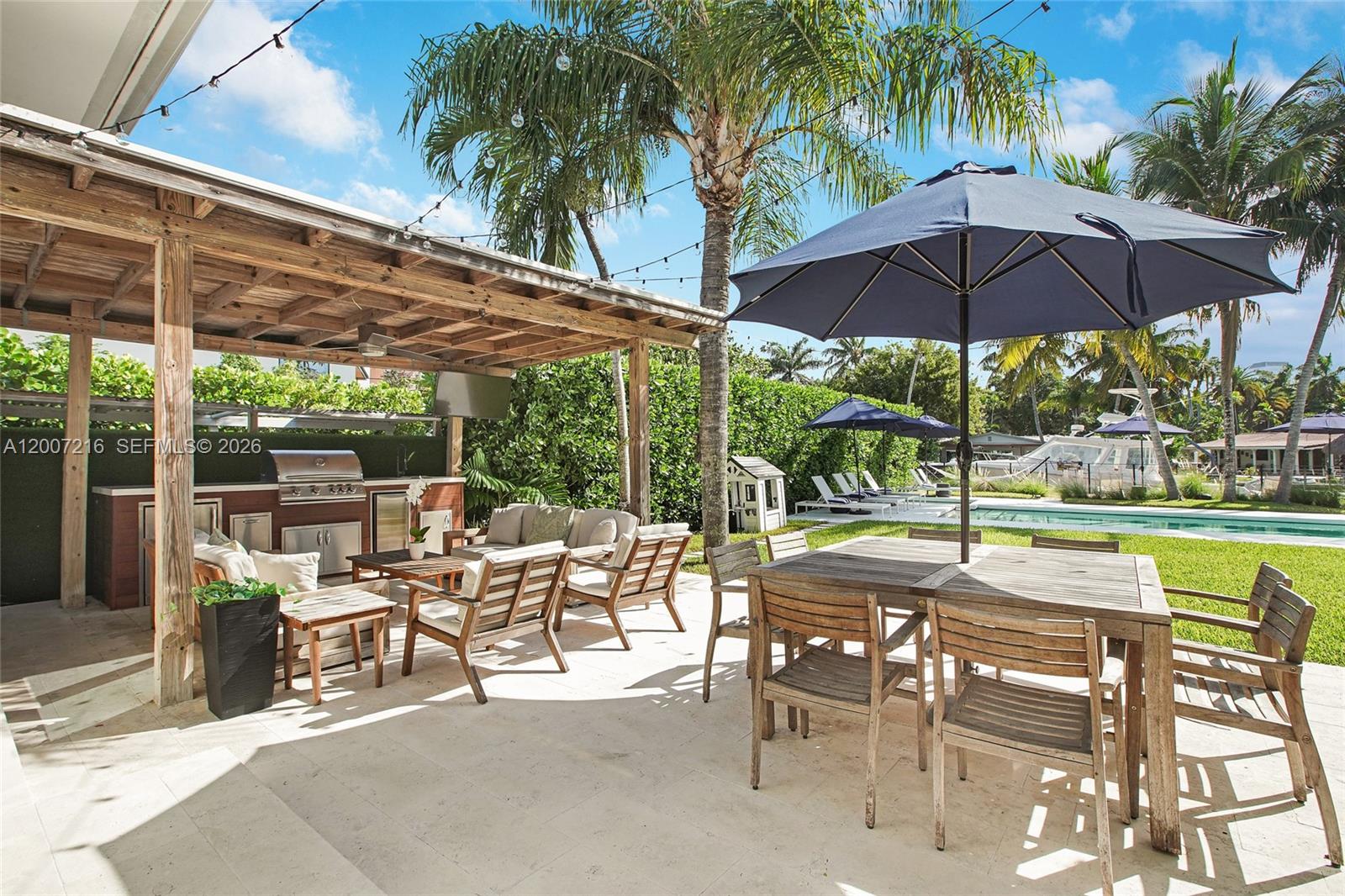 A covered outdoor patio features a kitchen, dining area, and lounge seating overlooking a pool — 815 NE 76th St, Miami FL 33138, MIAMI, FL