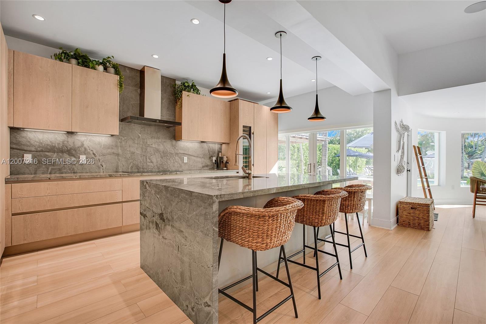 A modern kitchen features light wood cabinetry, a large stone island, and three pendant lights — 815 NE 76th St, Miami FL 33138, MIAMI, FL