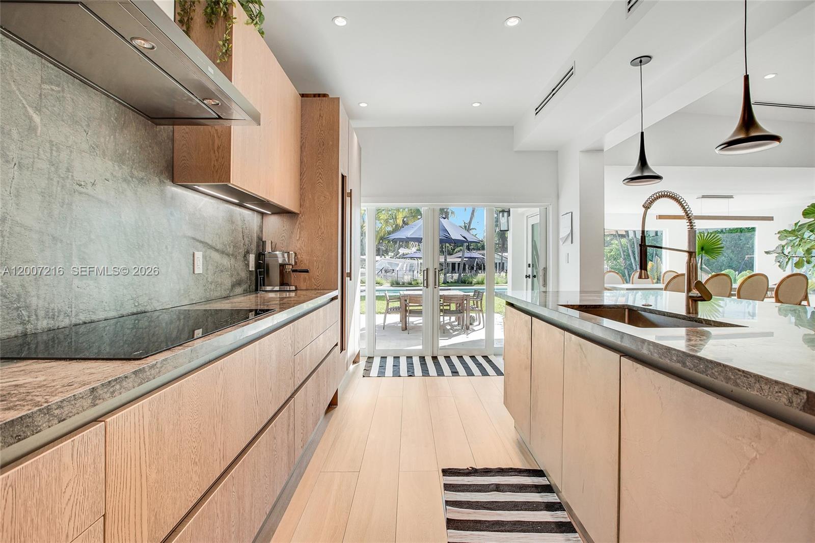 A modern kitchen features light wood cabinetry, stone countertops, and a view of a pool — 815 NE 76th St, Miami FL 33138, MIAMI, FL
