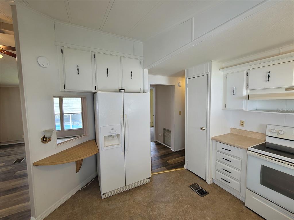 A kitchen features white cabinets, a side-by-side refrigerator, a stove, and a small wooden shelf — 7209 EL MEYERS STREET, ZEPHYRHILLS, FL