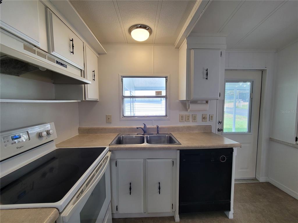 A kitchen features white cabinets, a double sink, a black dishwasher, and a white stove — 7209 EL MEYERS STREET, ZEPHYRHILLS, FL
