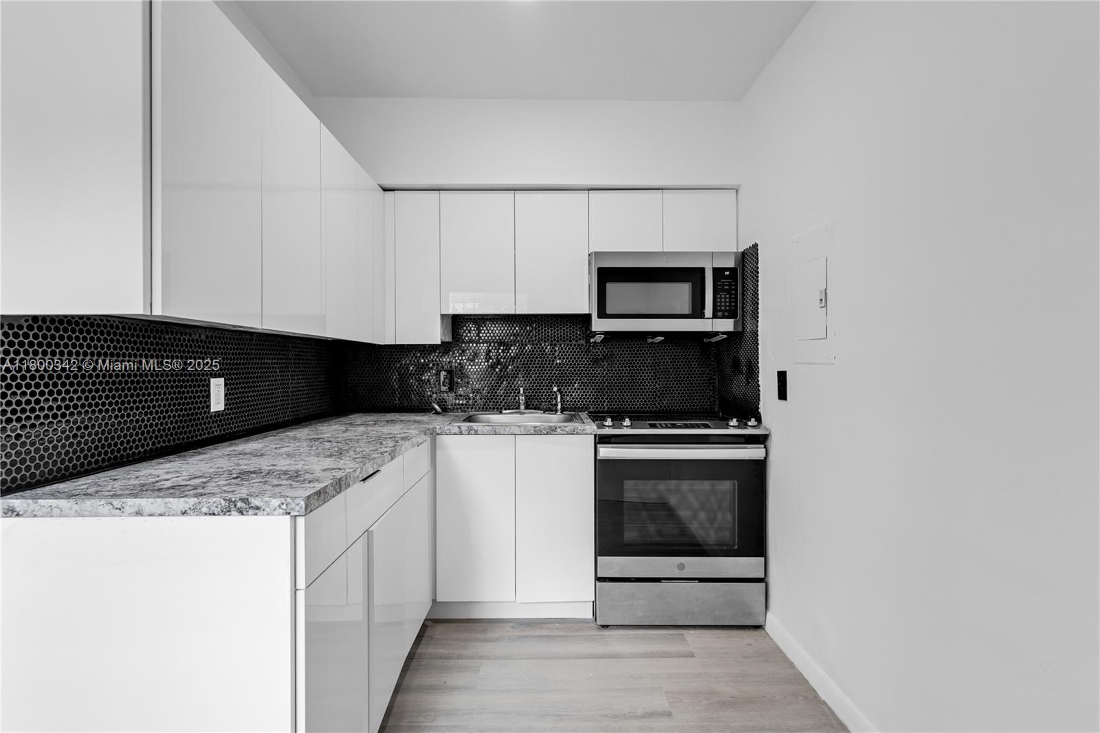 A modern kitchen features white cabinets, a black honeycomb backsplash, and a granite countertop — 46 NW 62nd St # 4, Miami FL 33150, MIAMI, FL