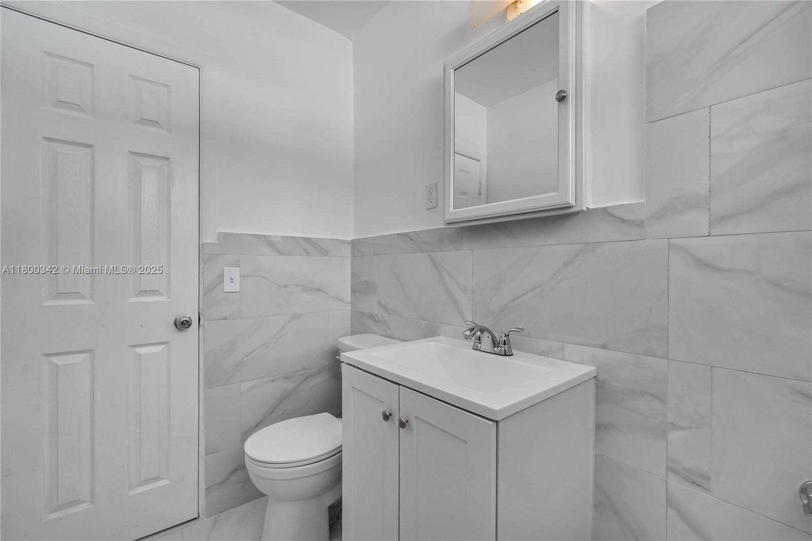 A bathroom features a white vanity, a toilet, and walls tiled with white marble — 46 NW 62nd St # 4, Miami FL 33150, MIAMI, FL