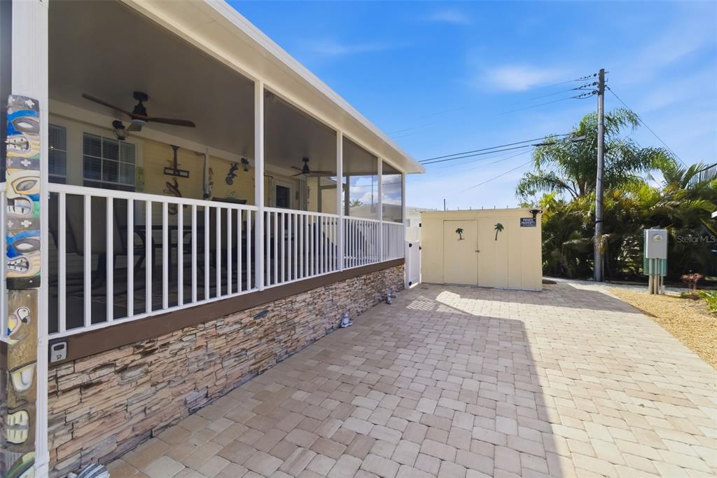 A screened-in porch with stone siding sits beside a paved patio and a storage shed — 812 50TH AVENUE TERRACE W, BRADENTON, FL