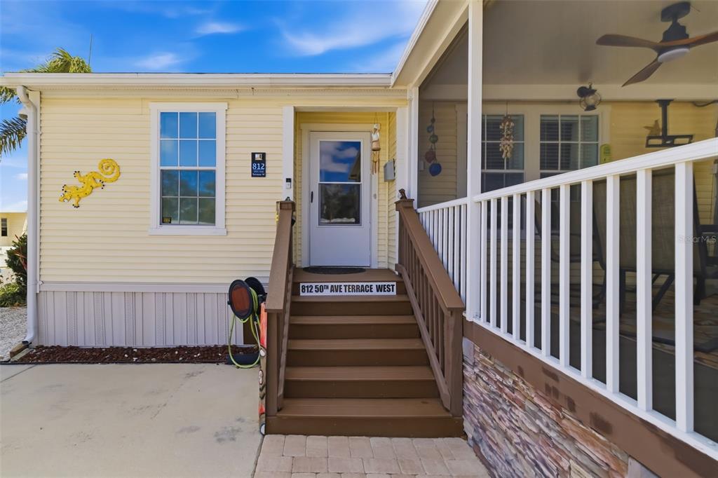 A yellow house exterior features a brown wooden staircase leading to a white front door — 812 50TH AVENUE TERRACE W, BRADENTON, FL