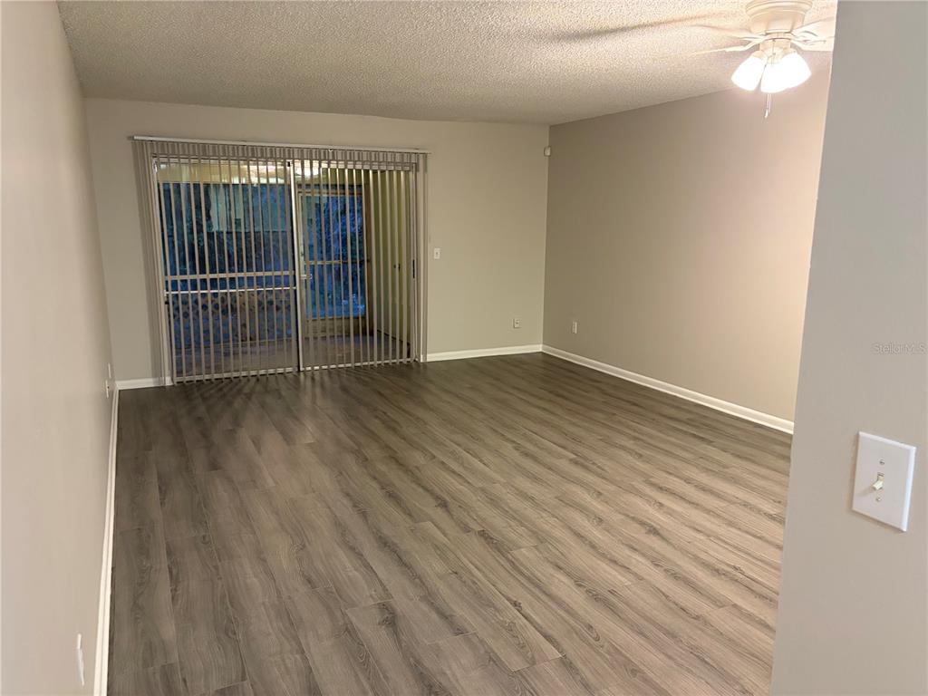An empty living room features wood-look flooring, light gray walls, and a sliding glass door — 7081 BALBOA DRIVE UNIT 7081, ORLANDO, FL