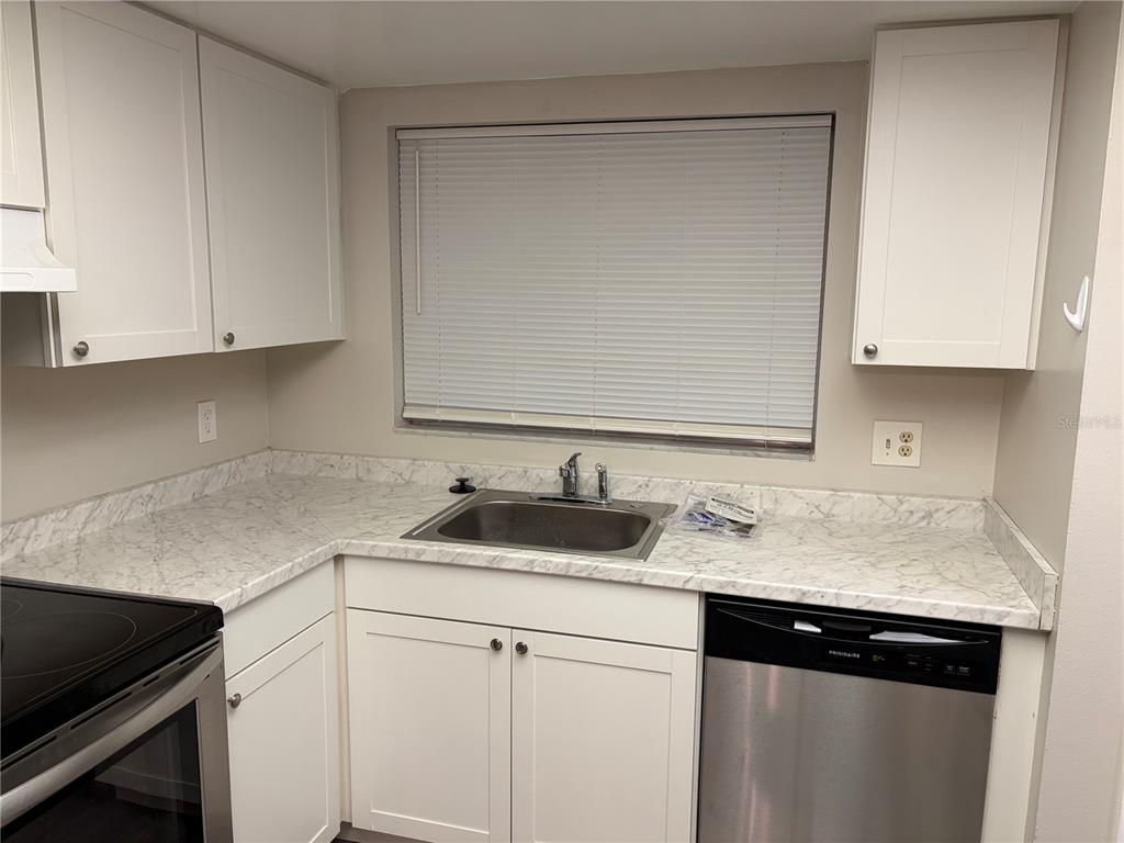 A kitchen features white cabinets, marble-patterned countertops, a stainless steel dishwasher, and a window — 7081 BALBOA DRIVE UNIT 7081, ORLANDO, FL