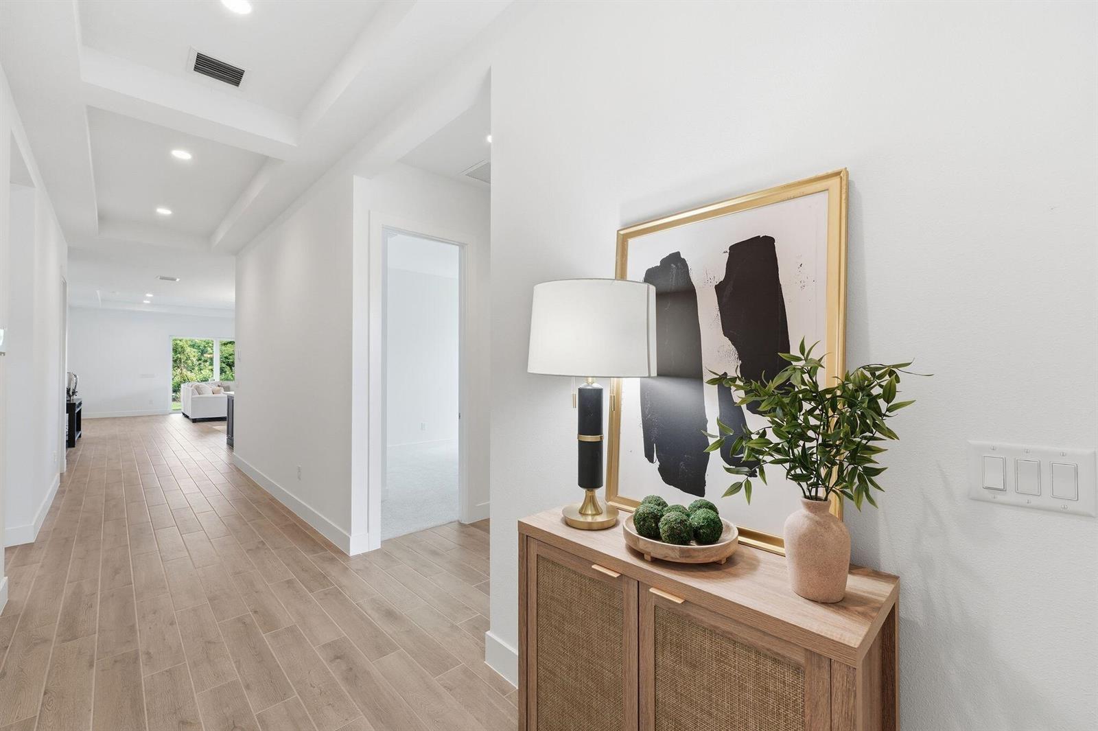 A bright hallway features light wood-look tile flooring, white walls, and a decorative entryway console — 6883 68th Square, Vero Beach FL 32967, VERO BEACH, FL