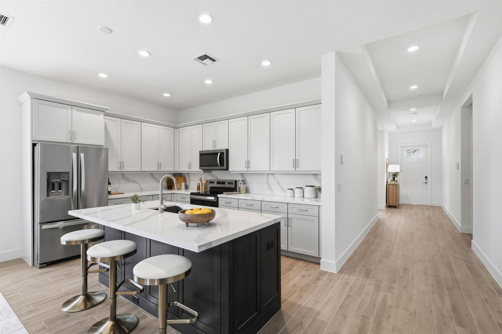 A modern kitchen features white cabinetry, a dark island with bar stools, and light flooring — 6883 68th Square, Vero Beach FL 32967, VERO BEACH, FL