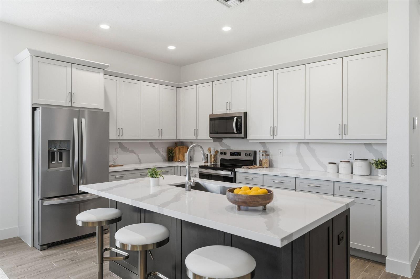 A modern kitchen features white upper cabinets, gray lower cabinets, and a large quartz island — 6883 68th Square, Vero Beach FL 32967, VERO BEACH, FL