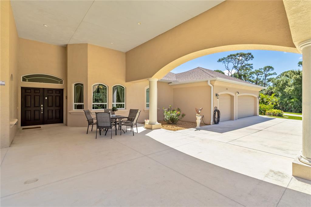 A covered patio features a dining set, arched openings, and an attached multi-car garage — 1991 HEASLEY ROAD, ENGLEWOOD, FL