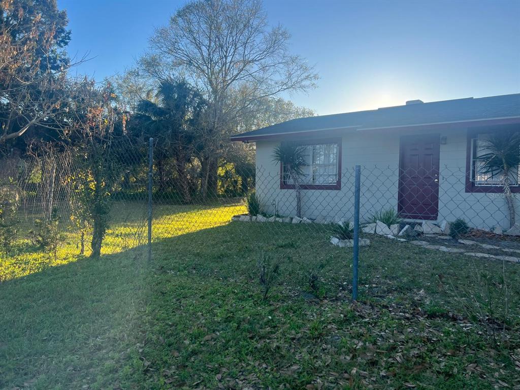 A single-story house with a maroon door and window trim viewed behind a chain-link fence — 1112/1114 S BAY AVENUE, SANFORD, FL
