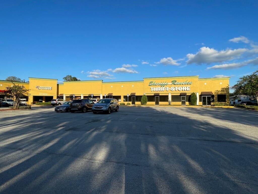 A yellow commercial strip mall building with a large parking lot under a blue sky — 27900 US HIGHWAY 27 HIGHWAY, LEESBURG, FL
