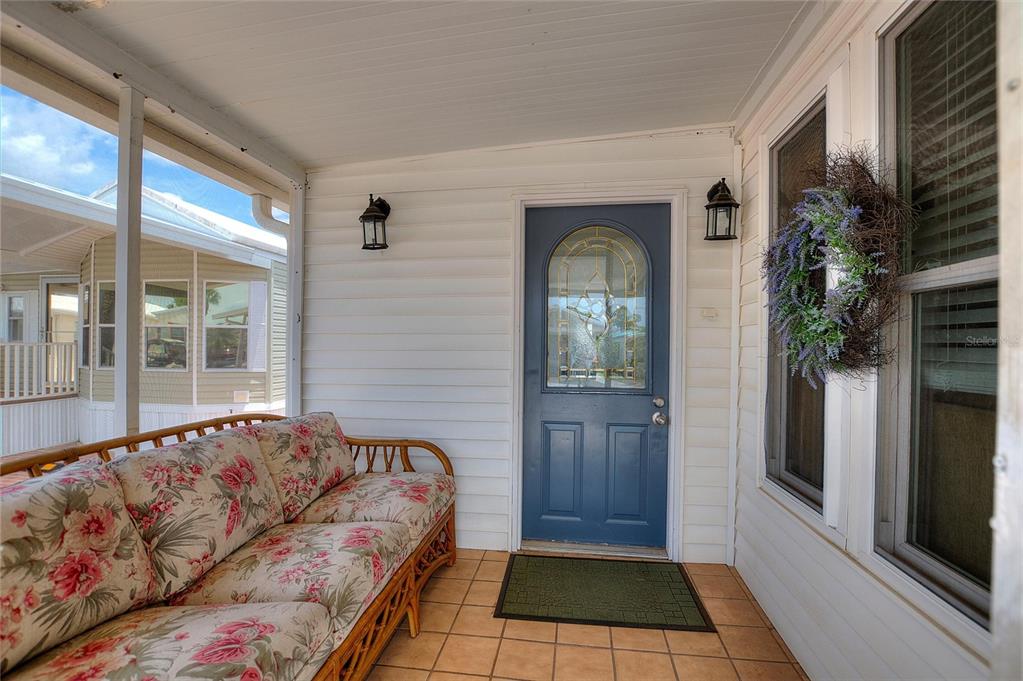 A covered porch features a floral sofa, a blue front door, and tiled flooring — 42769 HIGHWAY 27 UNIT 101, DAVENPORT, FL