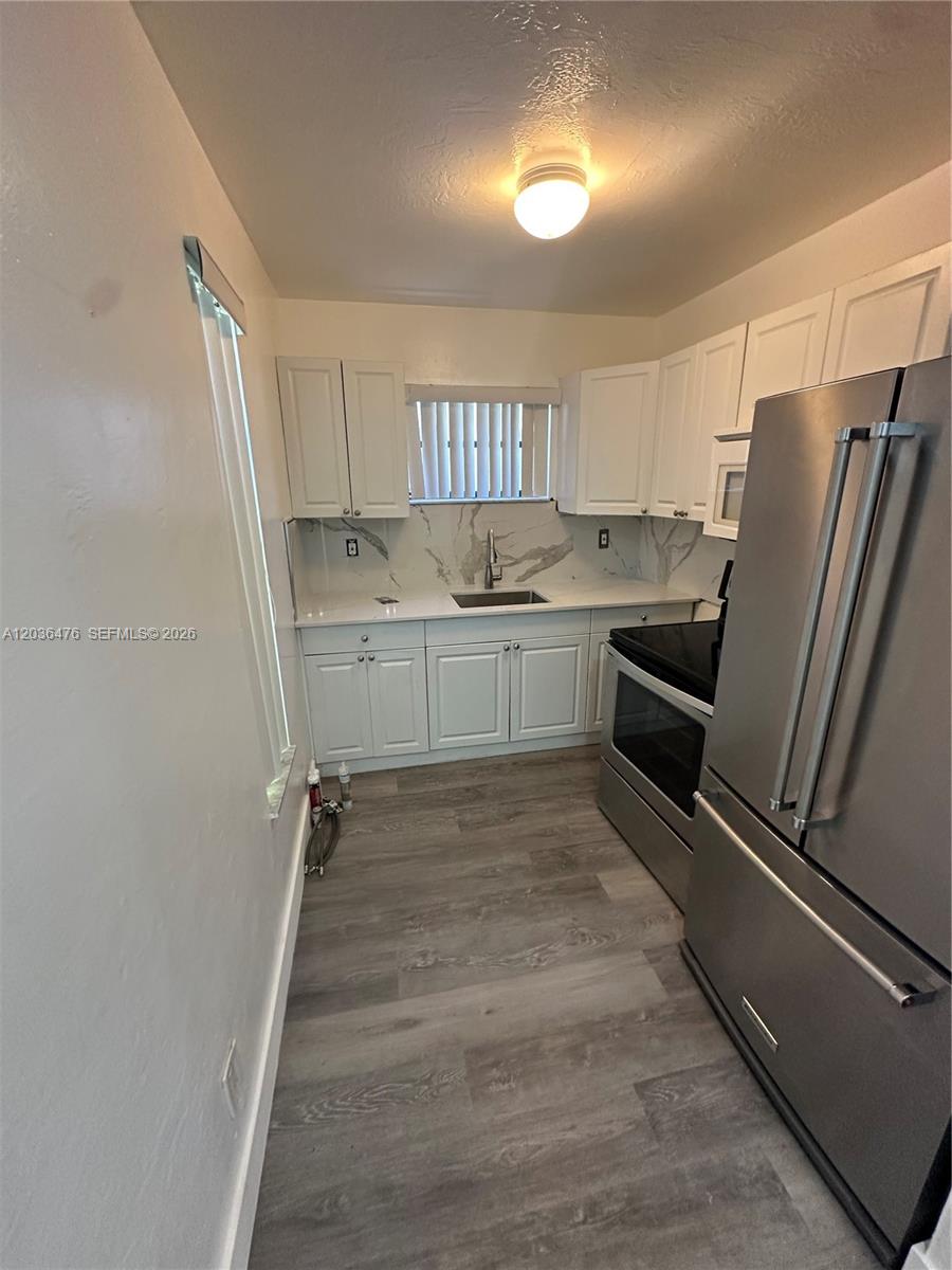 A small kitchen features white cabinets, stainless steel appliances, and marble-patterned countertops — 1670 Harding St # A, Hollywood FL 33020, HOLLYWOOD, FL