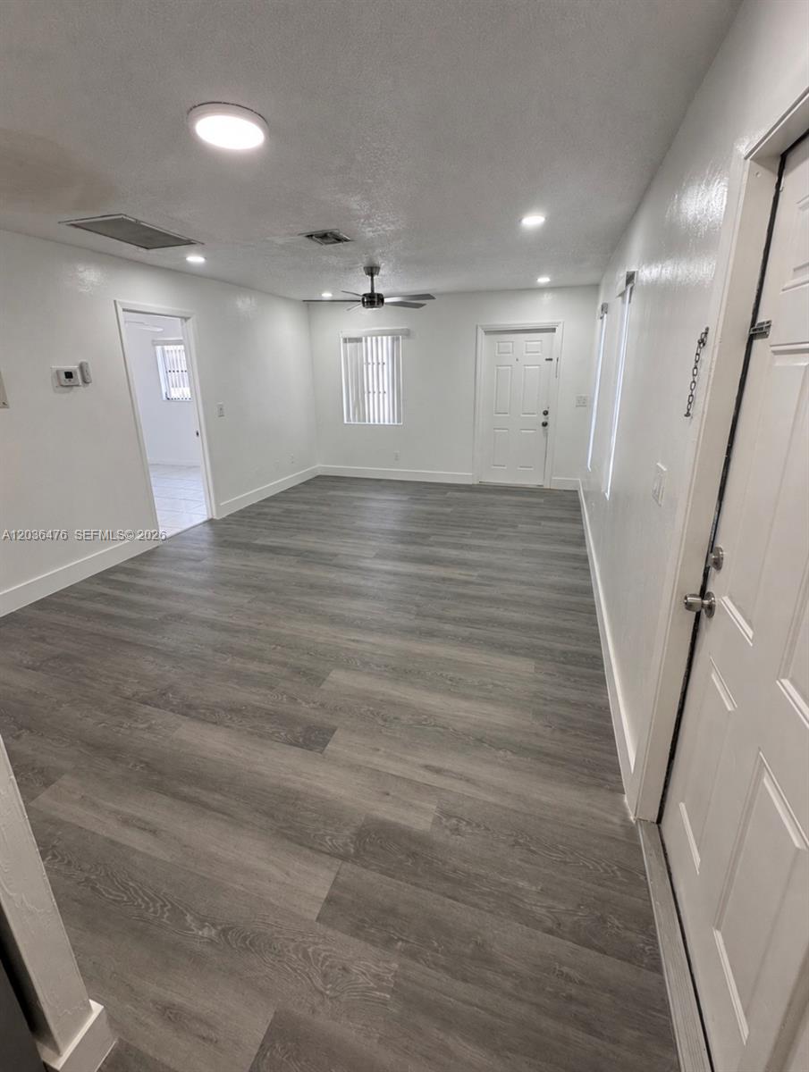 An empty room features gray wood-look flooring, white walls, a ceiling fan, and two doors — 1670 Harding St # A, Hollywood FL 33020, HOLLYWOOD, FL