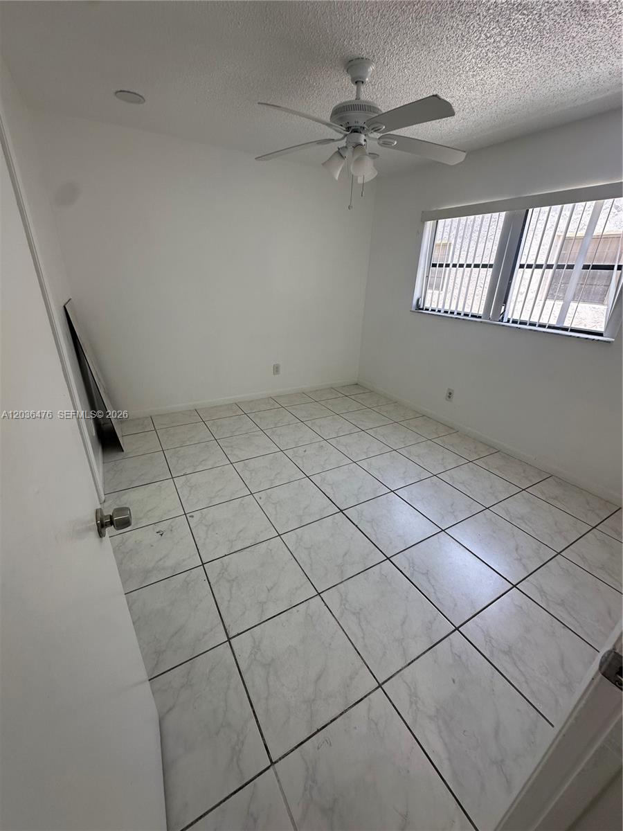 An empty bedroom features white walls, a ceiling fan, and light-colored tiled flooring — 1670 Harding St # A, Hollywood FL 33020, HOLLYWOOD, FL