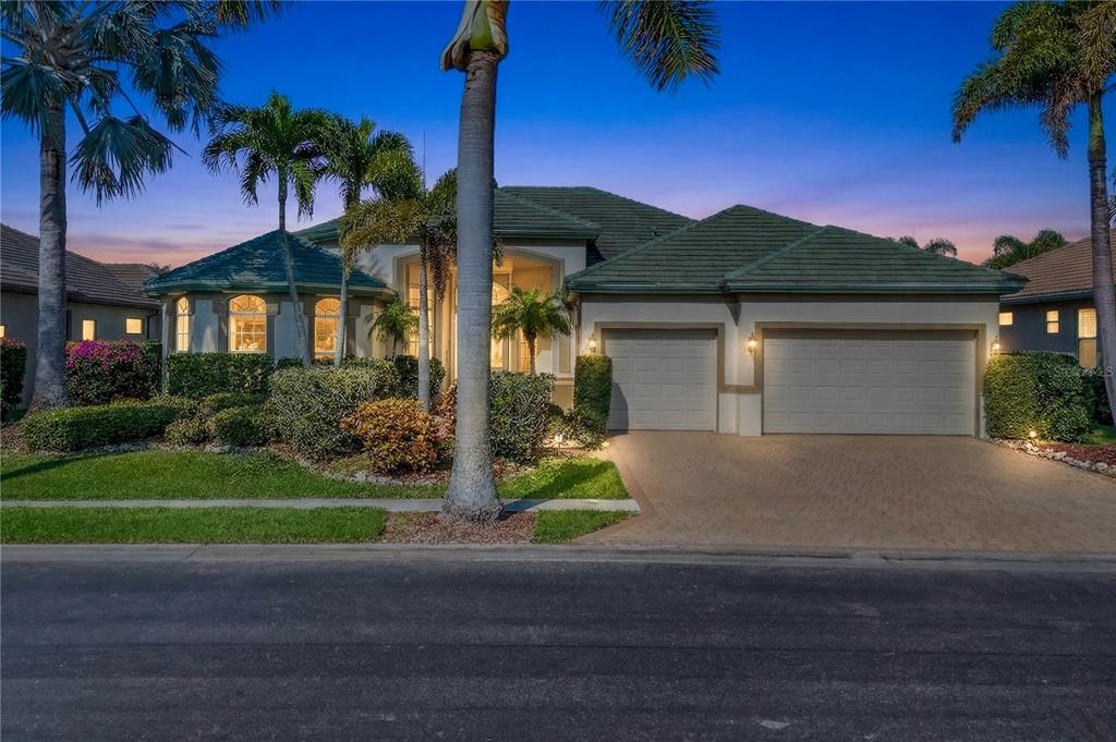 A single-story house with a green tile roof, two-car garage, and palm trees at dusk — 15930 CATALPA COVE DRIVE, FORT MYERS, FL