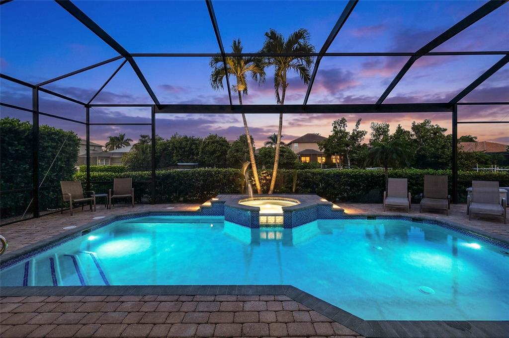 A swimming pool with an integrated spa sits inside a screened-in patio at sunset — 15930 CATALPA COVE DRIVE, FORT MYERS, FL