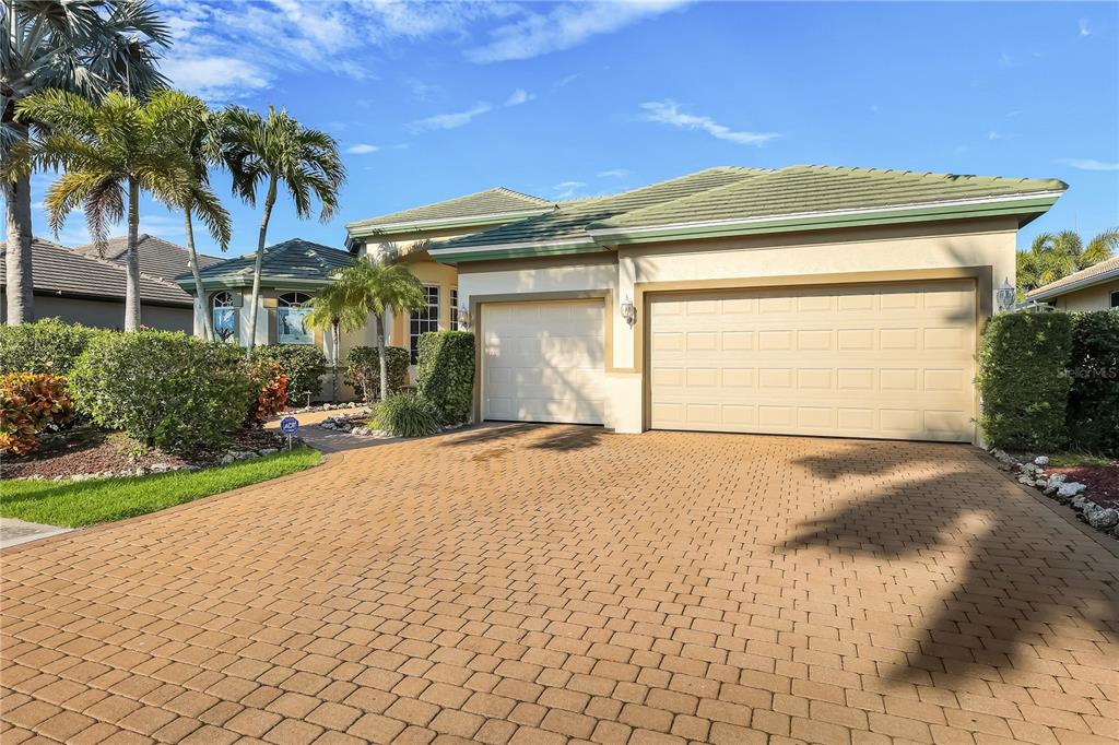 A beige house with a green tile roof and a paved driveway features a three-car garage — 15930 CATALPA COVE DRIVE, FORT MYERS, FL