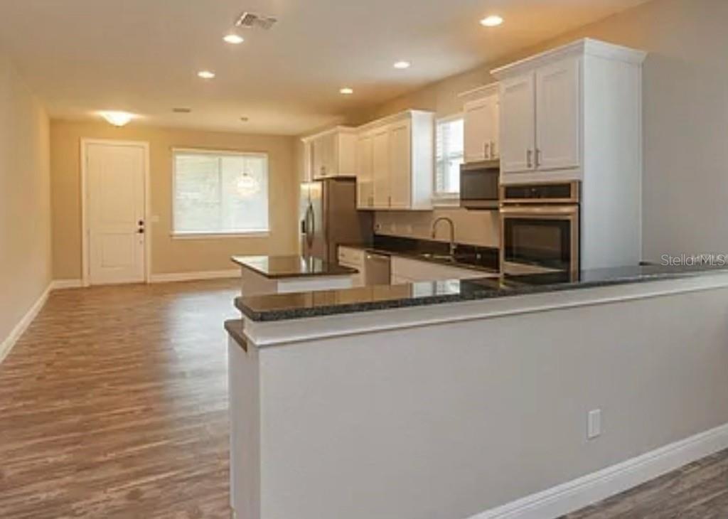 A kitchen with white cabinets, dark countertops, and stainless steel appliances overlooks an open living area — 0 FISHER LANE WAY, OCKLAWAHA, FL