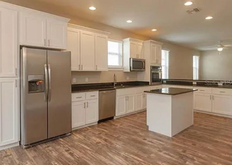 A kitchen features white cabinets, stainless steel appliances, a center island, and wood-look flooring — 0 FISHER LANE WAY, OCKLAWAHA, FL