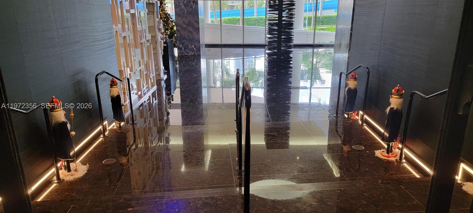 A staircase with dark marble flooring and decorative nutcracker statues leads toward a glass-walled lobby — 1850 S Ocean Dr # 3007, Hallandale Beach FL 33009, HALLANDALE BEACH, FL