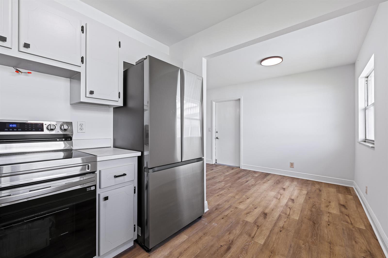 A kitchen with white cabinets, stainless steel appliances, and wood-look flooring leads into a dining area — 613 Monaco M, Delray Beach FL 33446, DELRAY BEACH, FL