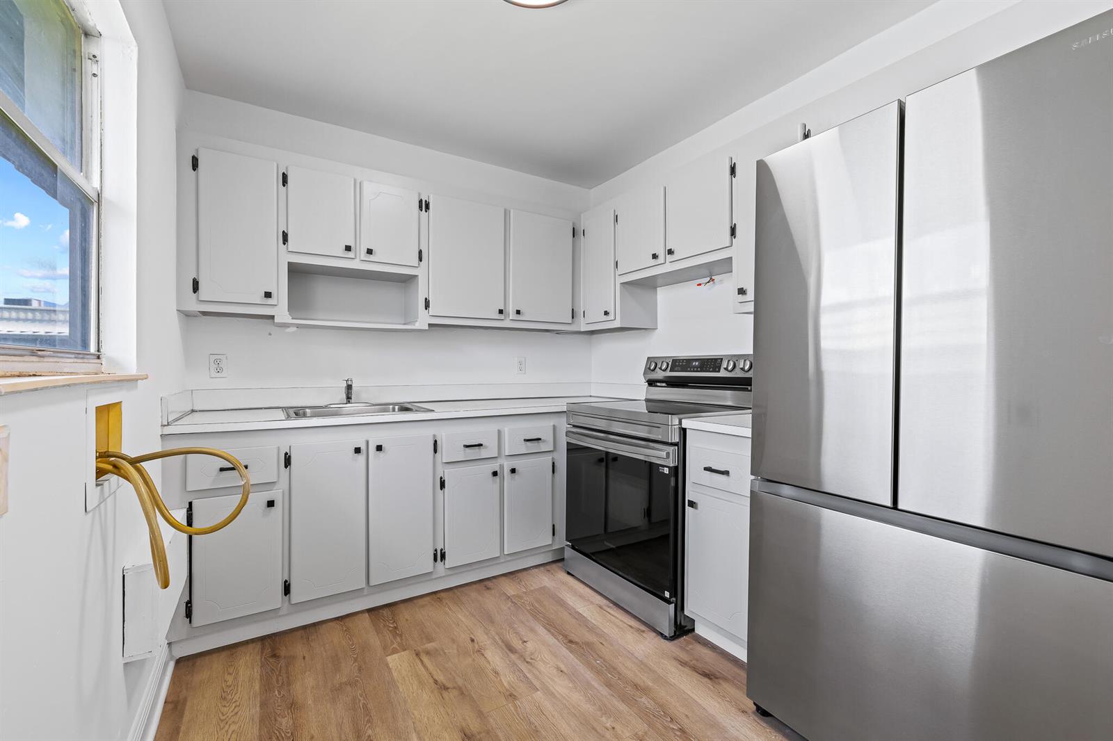 A kitchen features white cabinets, stainless steel appliances, a sink, and light wood-look flooring — 613 Monaco M, Delray Beach FL 33446, DELRAY BEACH, FL