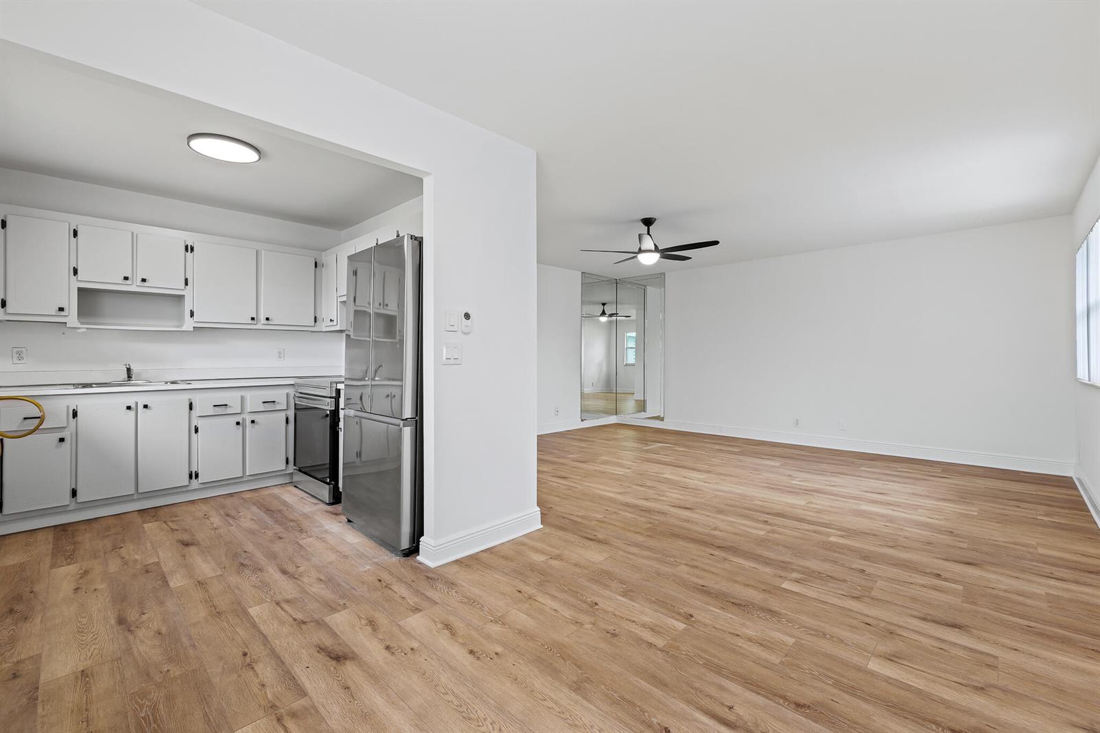 A kitchen with white cabinets and stainless steel appliances opens into a spacious living area — 613 Monaco M, Delray Beach FL 33446, DELRAY BEACH, FL