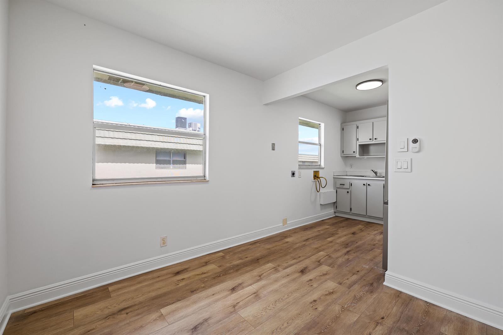 A room with wood-look flooring leads to a small kitchen area with white cabinets — 613 Monaco M, Delray Beach FL 33446, DELRAY BEACH, FL