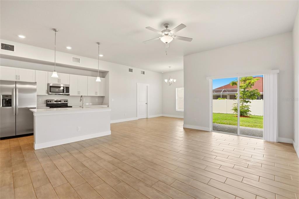 A bright open-concept kitchen and living area with light wood-look tile flooring and sliding doors — 870 COLUMBIA STREET, PORT CHARLOTTE, FL