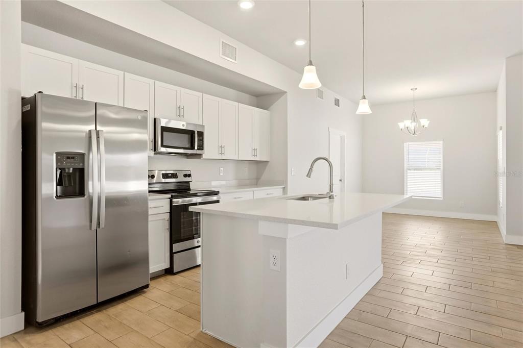 A modern kitchen features white cabinetry, stainless steel appliances, a center island, and wood-look flooring — 870 COLUMBIA STREET, PORT CHARLOTTE, FL
