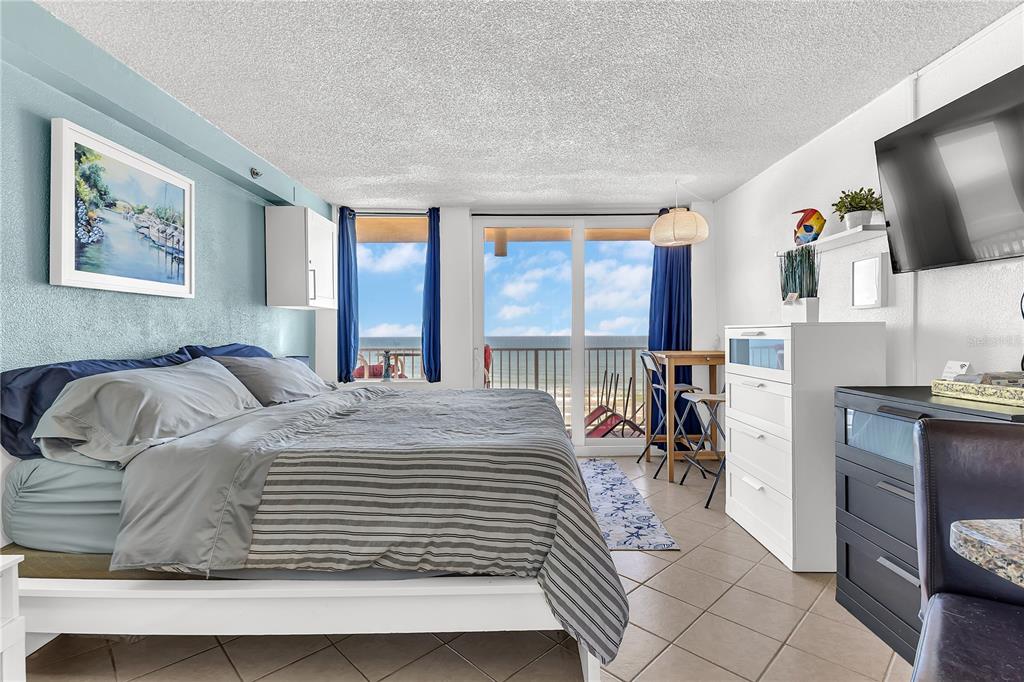 A bedroom with a king bed, tiled floors, and a balcony overlooking the ocean — 701 S ATLANTIC AVENUE UNIT 508, DAYTONA BEACH, FL