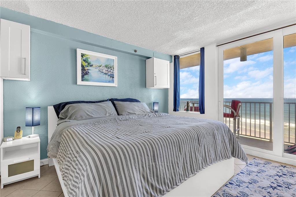 A bedroom features a bed with striped bedding, blue walls, and a balcony overlooking the ocean — 701 S ATLANTIC AVENUE UNIT 508, DAYTONA BEACH, FL