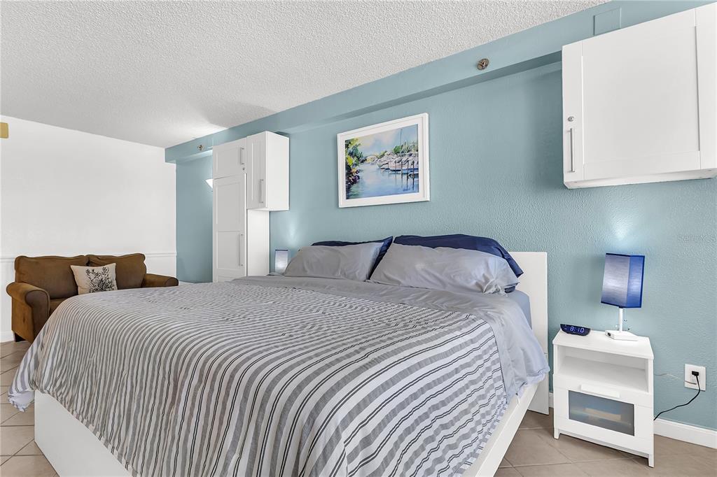 A bedroom features a bed with a striped comforter, white cabinetry, and a brown sofa — 701 S ATLANTIC AVENUE UNIT 508, DAYTONA BEACH, FL