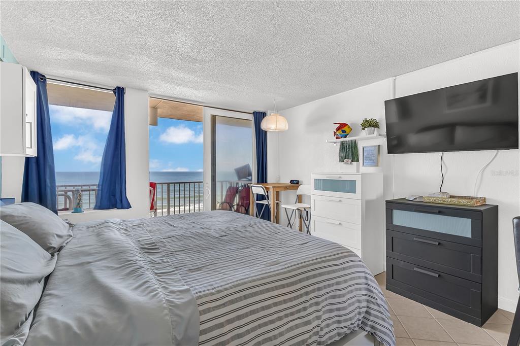 A bedroom with a bed, a television, a dresser, and a balcony overlooking the ocean — 701 S ATLANTIC AVENUE UNIT 508, DAYTONA BEACH, FL