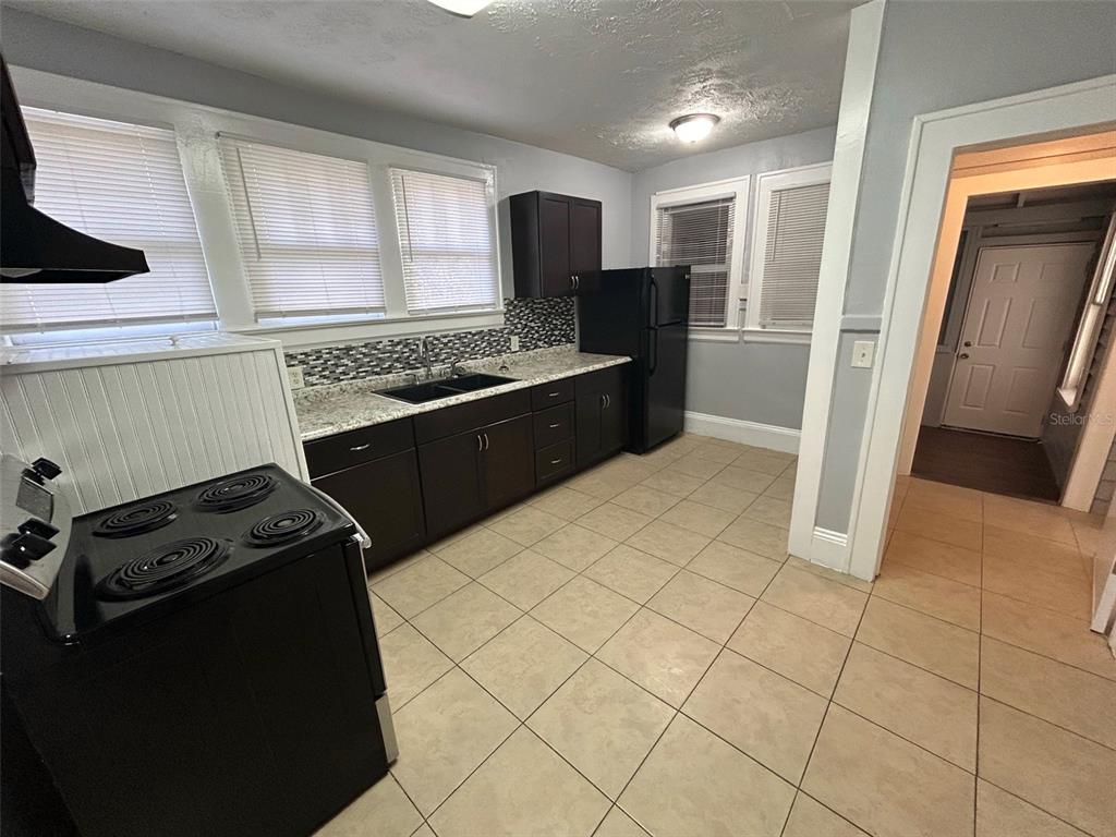 A kitchen features dark cabinets, granite countertops, a black stove, and light-colored tile flooring — 524 BASSWOOD STREET, JACKSONVILLE, FL