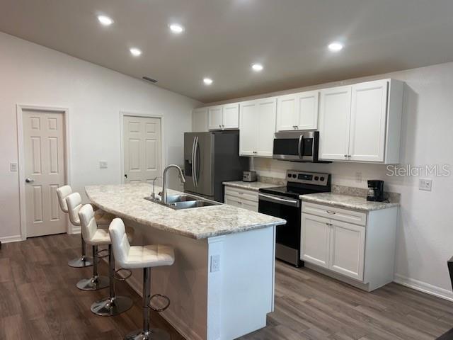 A kitchen features white cabinetry, a granite-topped island with bar stools, and stainless steel appliances — 4363 SWAN STREET, HAINES CITY, FL
