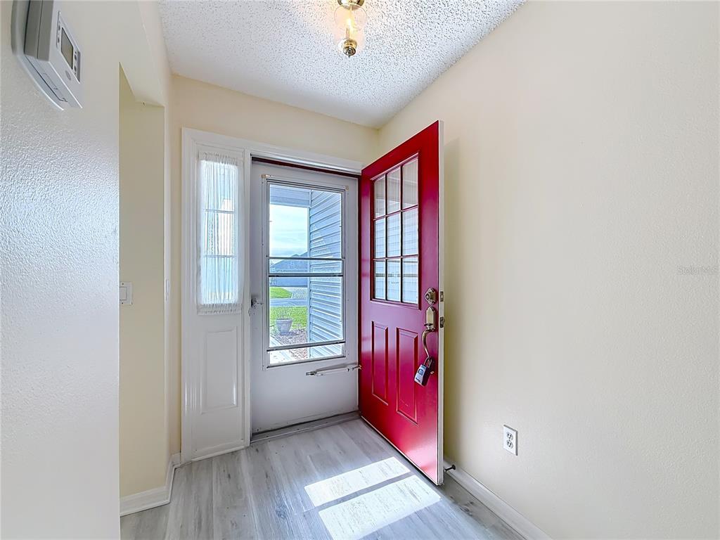 An entryway features light wood-look flooring, a red front door, and a white storm door — 2129 ZARAGOZA PLACE, THE VILLAGES, FL