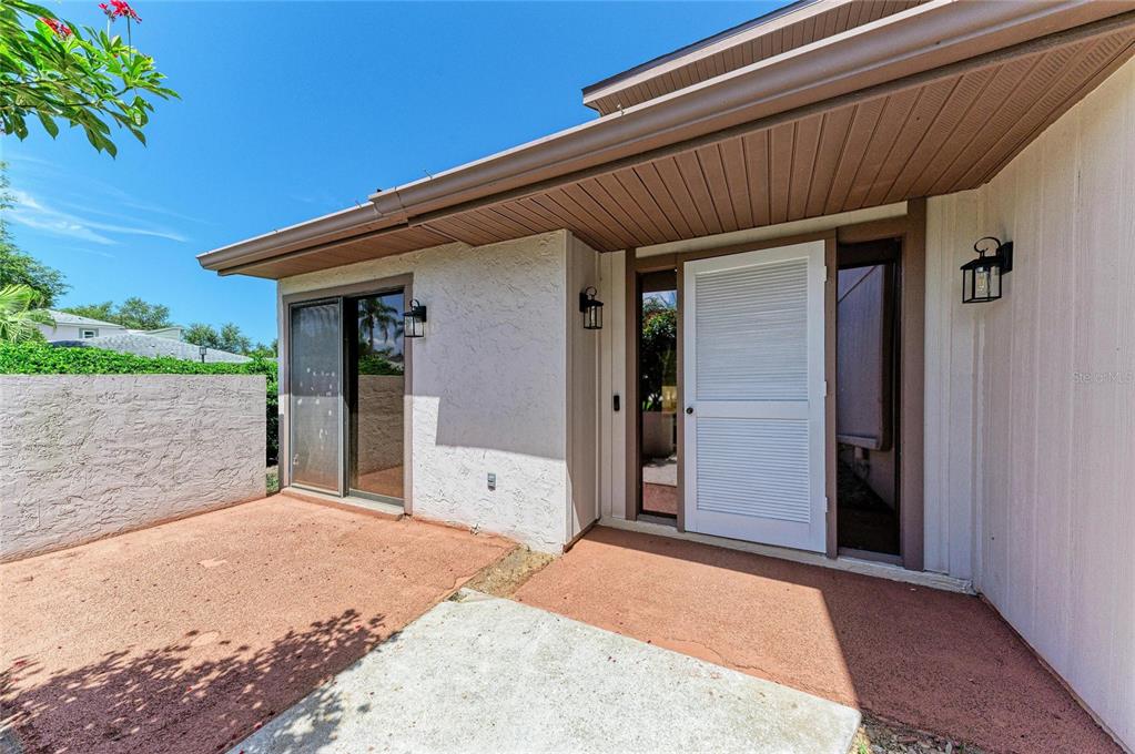 A white front door with sidelights and a sliding glass door on a concrete patio — 4515 WINSTON LANE N UNIT 47, SARASOTA, FL