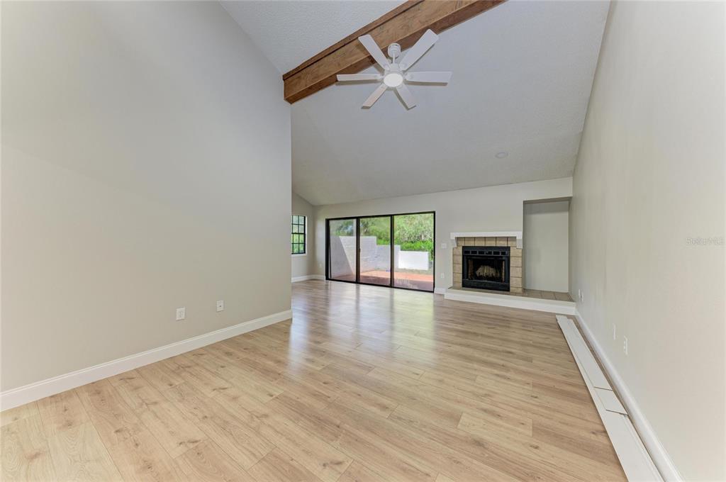 A living room with light wood flooring, a vaulted ceiling, a fireplace, and sliding glass doors — 4515 WINSTON LANE N UNIT 47, SARASOTA, FL