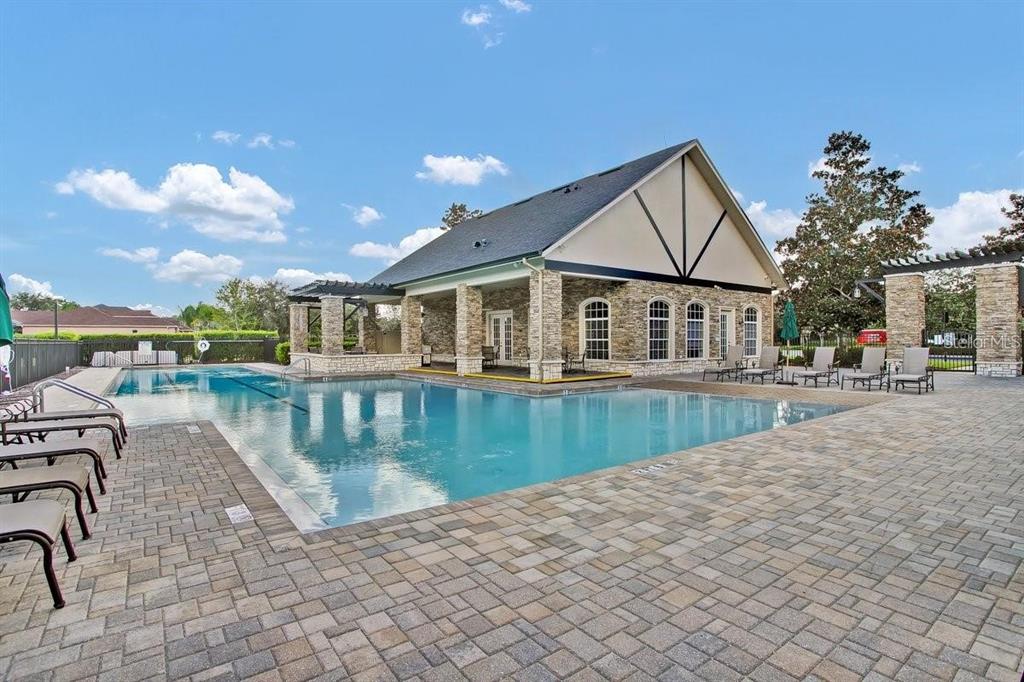 A swimming pool sits in front of a stone-clad clubhouse with a covered patio area — 3303 STONEGATE FALLS DRIVE, LAND O LAKES, FL