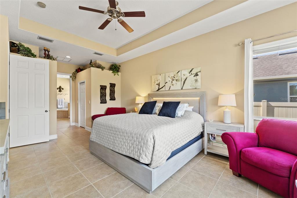 A bedroom features a tray ceiling, tile flooring, a king bed, and a pink armchair — 3303 STONEGATE FALLS DRIVE, LAND O LAKES, FL