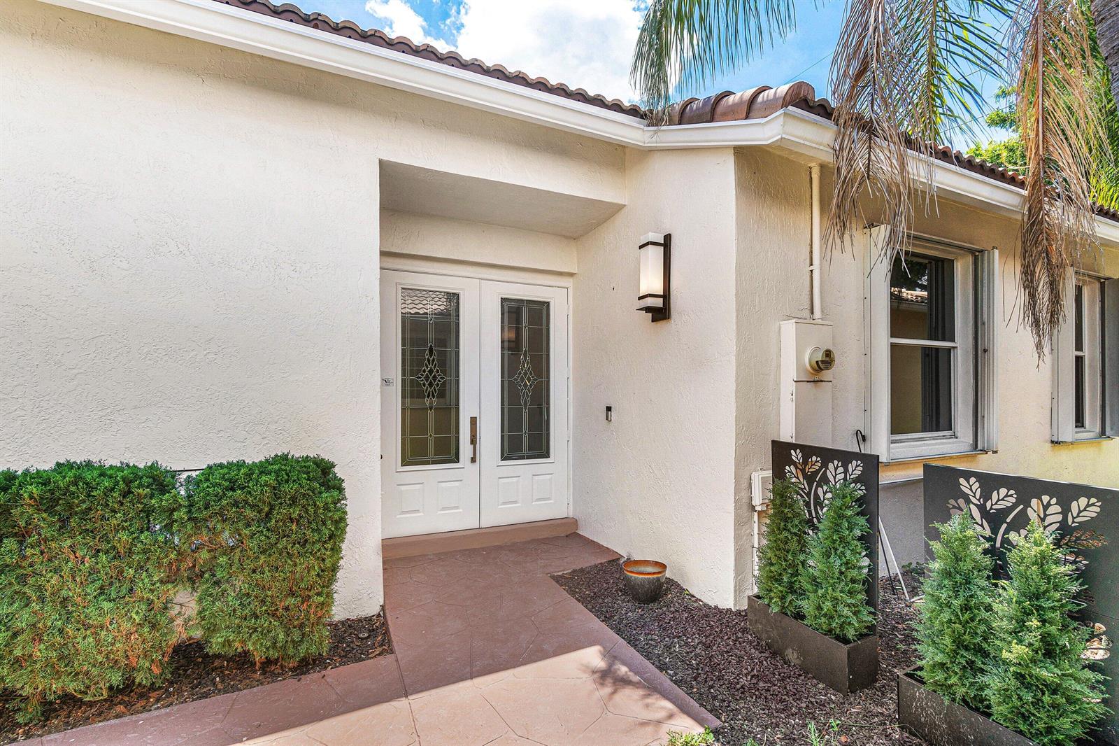 A white house exterior features a double front door, a tiled walkway, and small shrubs — 10817 Fillmore Drive, Boynton Beach FL 33437, BOYNTON BEACH, FL