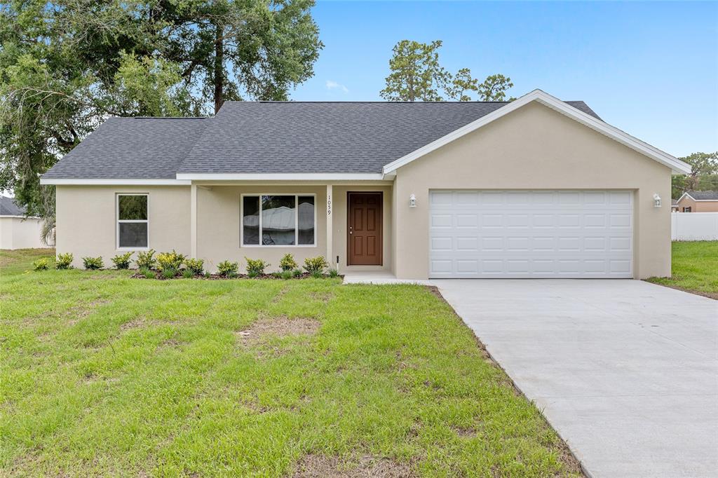 A single-story house with a beige stucco exterior, a dark roof, and a two-car garage — 22870 SW LIME RIDGE LANE, DUNNELLON, FL