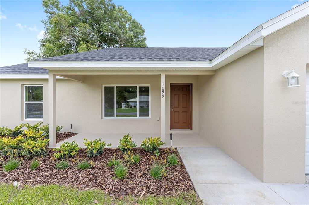A beige house exterior features a covered front porch, a brown door, and landscaping — 22870 SW LIME RIDGE LANE, DUNNELLON, FL